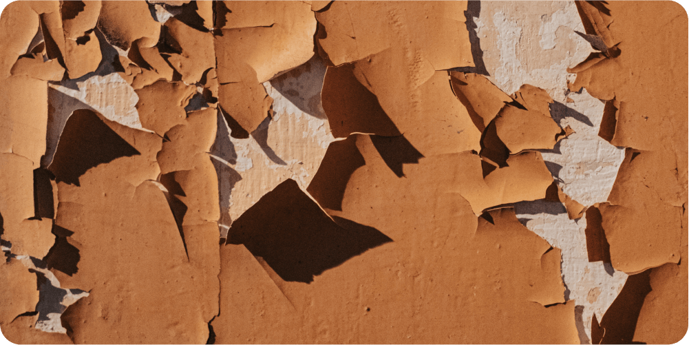 Под облупившейся коричневой краской на стене проступают белые пятна, создающие абстрактный, фактурный узор. Изображение передаёт ощущение упадка и времени.